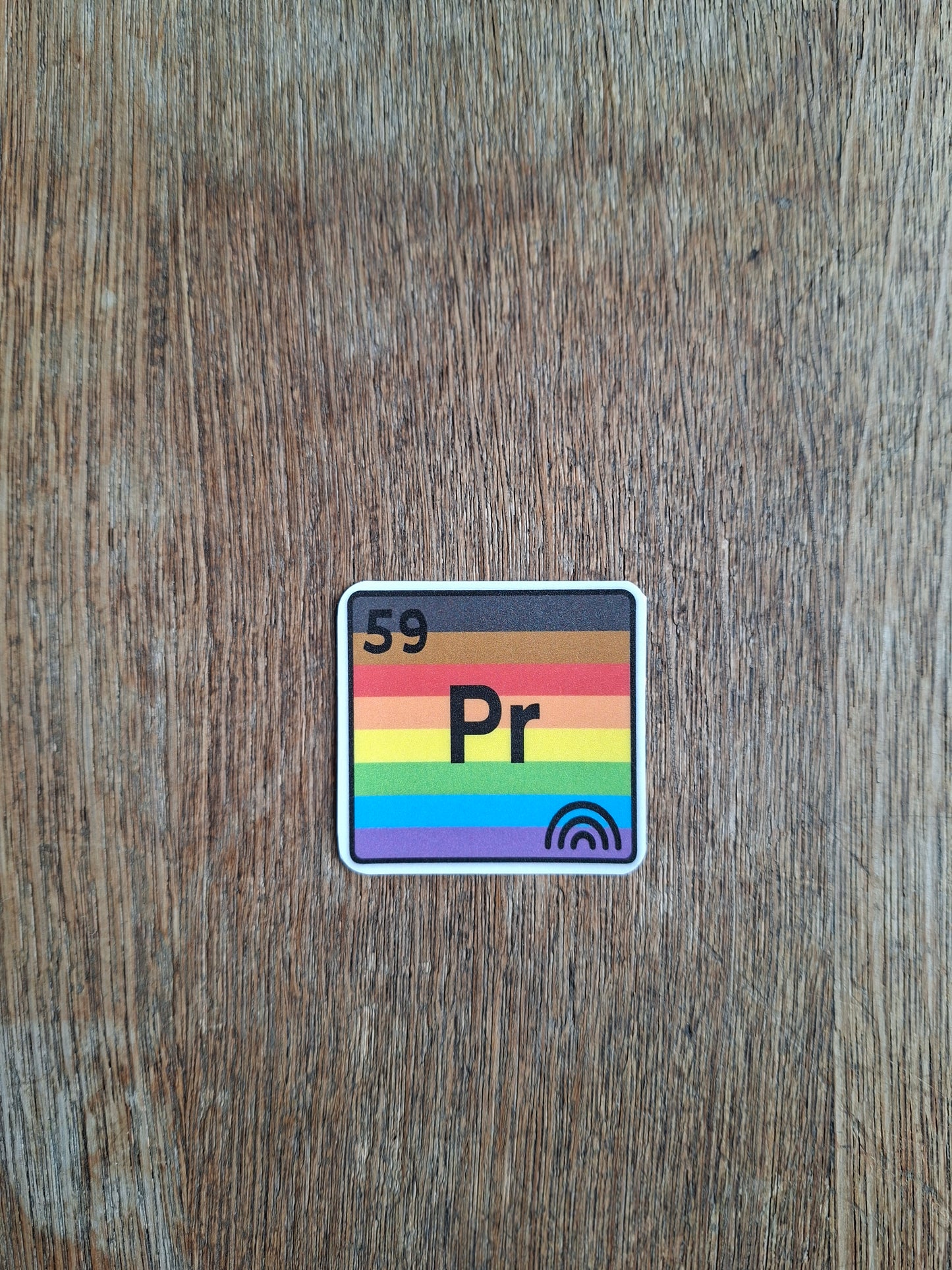Sticker with rainbow design and 'Pr' text on a wooden surface