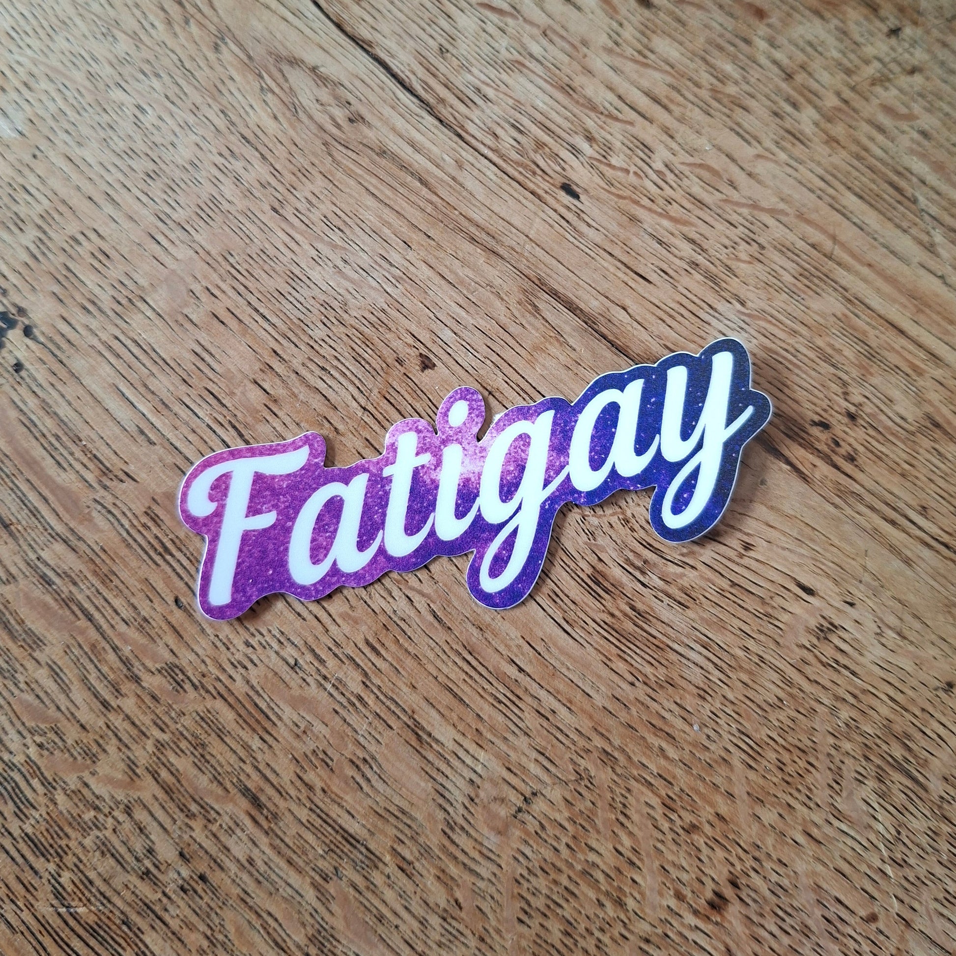 Sticker with 'Fatigay' text on a wooden surface