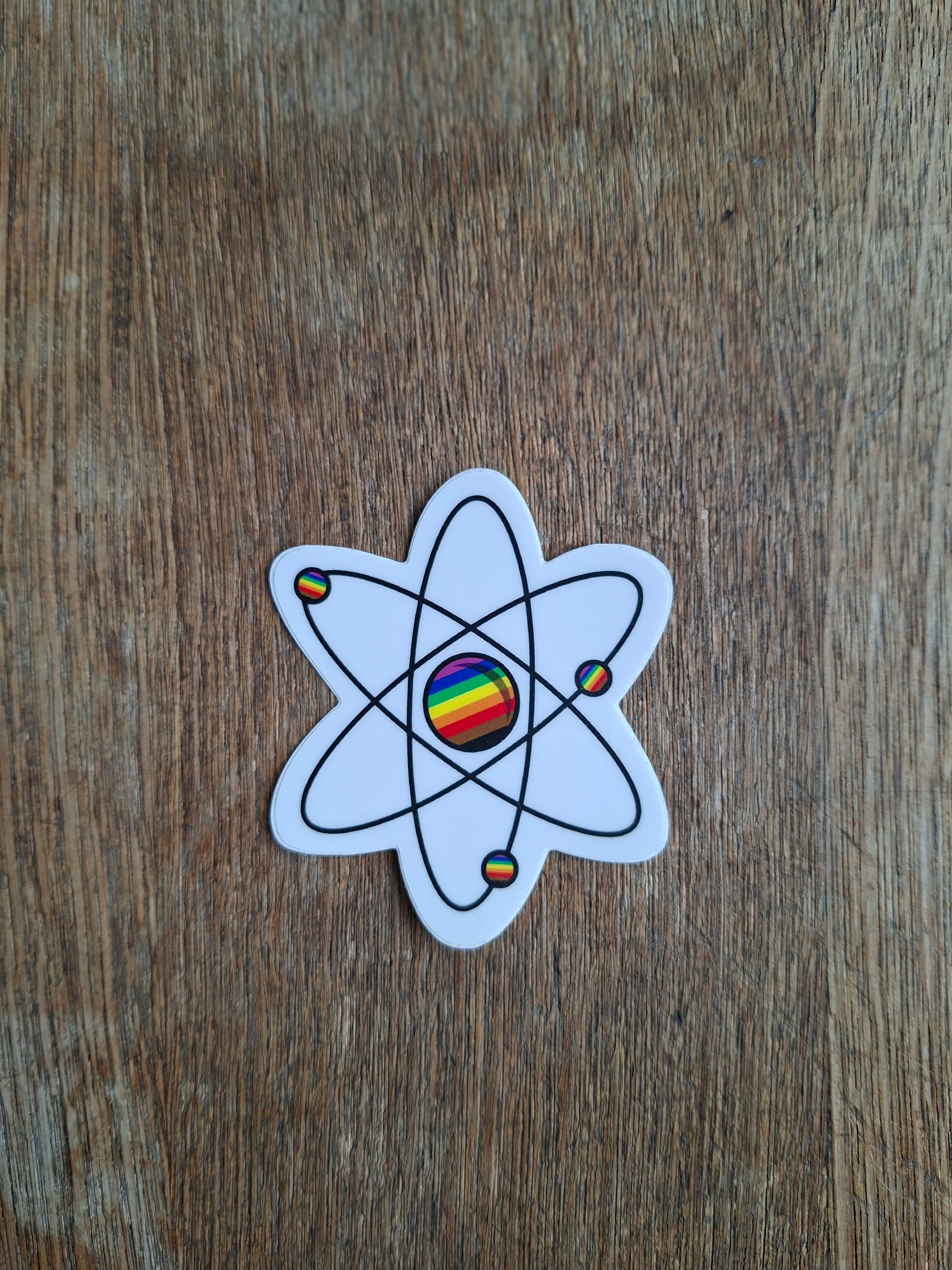 Atom symbol sticker with rainbow colors on a wooden surface