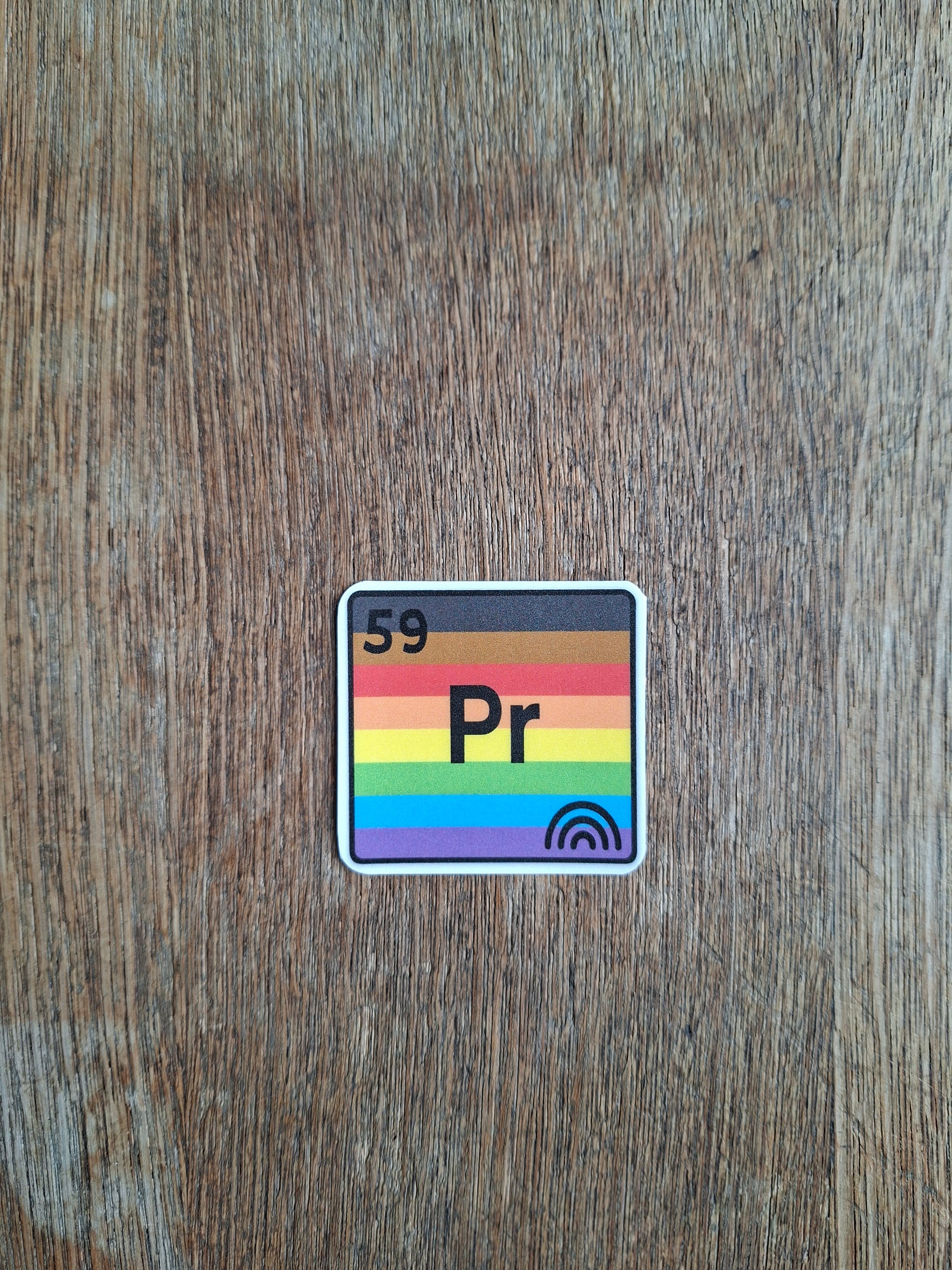 Sticker with rainbow design and 'Pr' text on a wooden surface