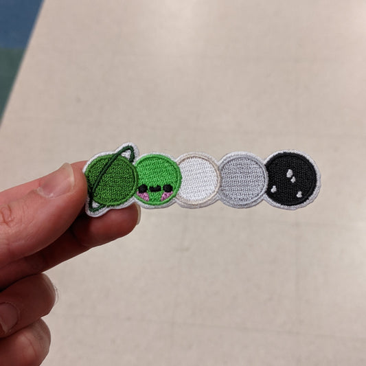 Hand holding an aromantic galaxy patch on a light colored background