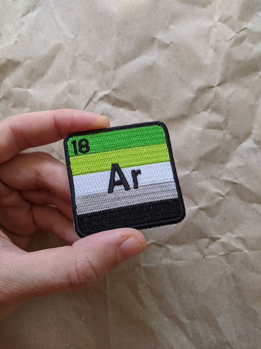 Hand holding a queer chemistry patch with atomic number 18 and symbol Ar on a crumpled paper background